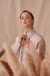 © Dmitry Tsvetkov - Tender soft studio portrait of elegant female model posing between ears of rye at textile background. Girl in brown skirt and beige jacket. Young woman with brunnette hair in pony tail