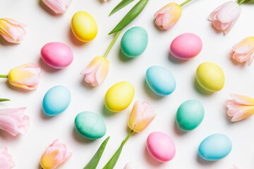 Easter layout of light pink and yellow spring flowers tulips and pastel colors eggs on a white background. Festive flat lay, happy easter concept.