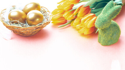 Wall Mural - Easter eggs gold. Golden colour egg in basket with spring tulips, white feathers on pastel pink background in Happy Easter decoration. Congratulatory easter design.