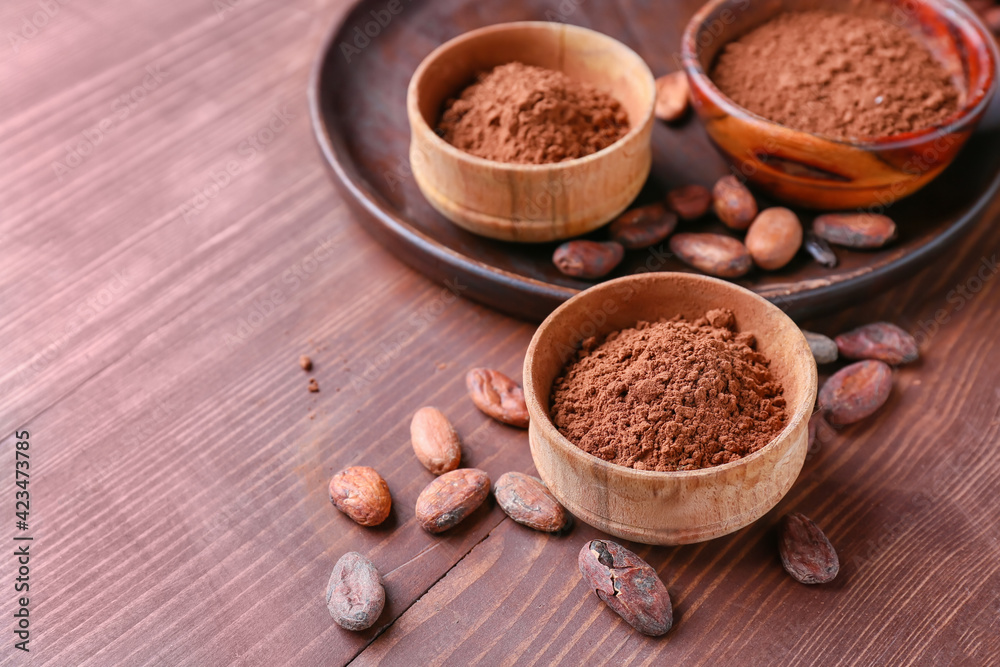 Bowls with cacao powder and beans on wooden background