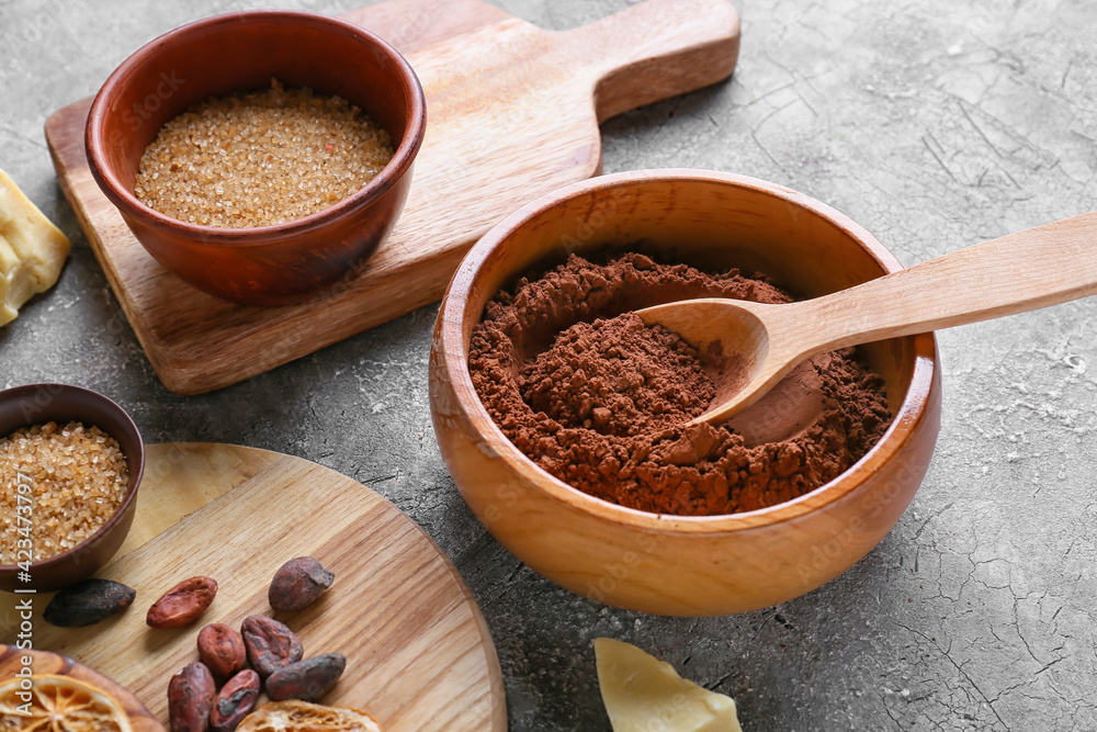 Bowls with cacao powder and sugar on grey background