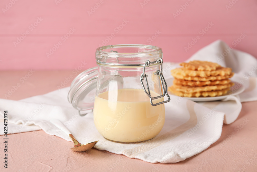 Jar with sweet condensed milk and waffles on color background