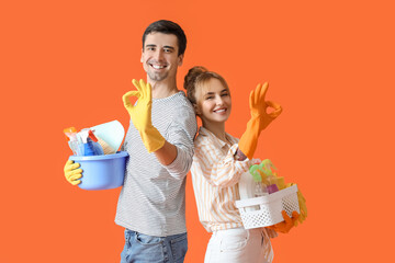 Wall Mural - Young couple with cleaning supplies showing OK on color background