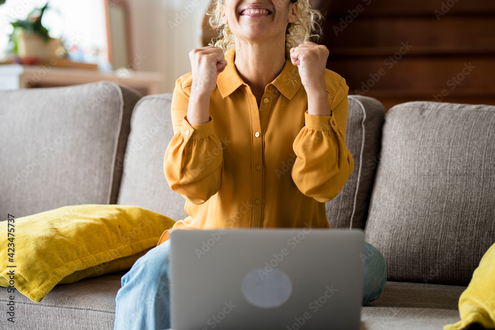 Happy adult woman receive notification on laptop computer and celebrate with joy - female people at home enjoy online technology - surprised middle age lady sitting on the sofa for news on pc notebook - obrazy, fototapety, plakaty 