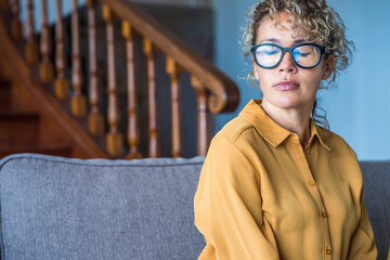 Closed eyes portrait sad expression young adult woman sitting alone on the sofa - depression disease and loneliness for caucasian female people - portrait of pretty woman with glasses