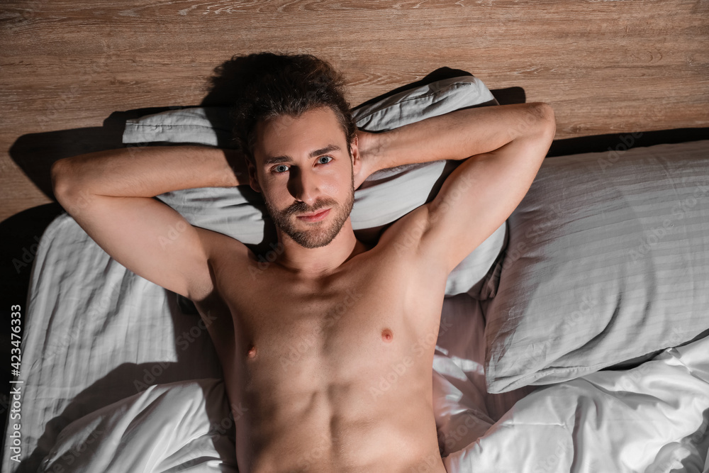 Sexy young man lying in bed at night