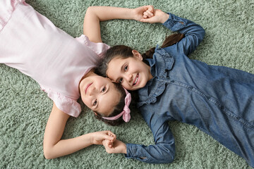 Poster - Portrait of cute twin girls lying on carpet, top view