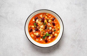 Vegetarian minestrone italian soup made with fresh vegetables, pasta and beans. Light gray background, top view