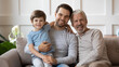 © fizkes - Portrait of three generations of Caucasian men sit relax on cozy couch in living room at home enjoying family weekend together. Happy smiling boy child with young father and elderly grandfather rest.