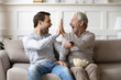© fizkes - Happy older Caucasian father and adult grownup son give high five celebrate win watching TV together. Overjoyed millennial man have fun enjoy at home with senior dad with football game.