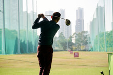 Rear View Of Asian Man Practicing Golf Swing At Driving Range