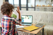 © Friends Stock - Online school. Rear view of latin school boy raising his hand during online lesson via video chat app. Child using laptop while studying at home