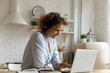 © fizkes - Happy young woman wear earphones look at laptop screen study online or take web course at home. Smiling female in headphones work distant on computer, use webcam digital conference application.