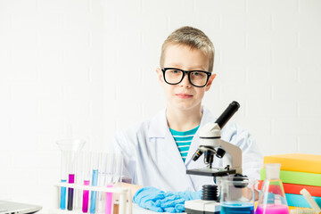 Wall Mural - a schoolboy with a microscope examines chemicals in test tubes, conducts experiments - a portrait on