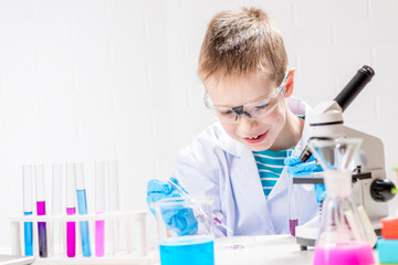 Wall Mural - a schoolboy with a microscope examines chemicals in test tubes, conducts experiments - a portrait on
