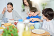 © Friends Stock - Cute little hispanic boy having breakfast together with his mom and siblings. Latin family enjoying meal together, sitting at the kitchen table at home