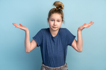 Confused teenage girl on a blue background spreads his arms. The girl gestures, shows that she does not know something.