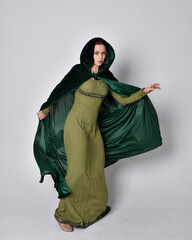 full length portrait of red haired girl wearing celtic, green medieval gown with fantasy velvet cloak. Standing pose isolated against a studio background.