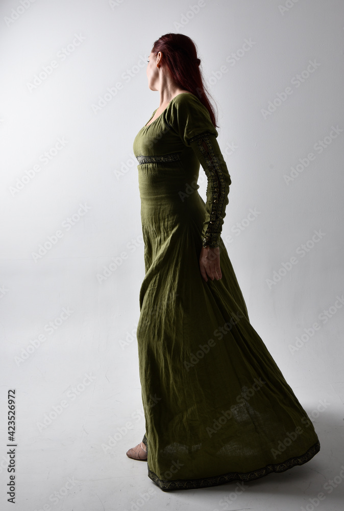 full length portrait of red haired girl wearing celtic, green medieval gown  with shadowy backlighting. Standing pose isolated against a studio  background. Stock Photo | Adobe Stock