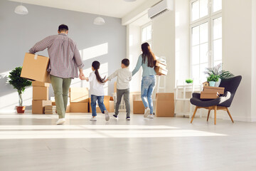 Rear view on father and mother holding cardboard boxes with belongings and children hands walking together entering to empty living room in new house. Happy family home moving day and relocation