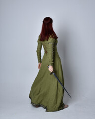 Canvas Print - full length portrait of red haired girl wearing celtic, green medieval gown. Standing pose, holding a sword, isolated against a studio background.