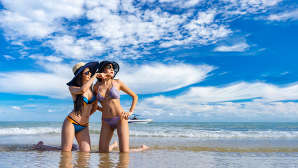 Wall Mural - Two young tourist bikini girls having fun on vacation at the beach on sunny day. Sexy Asian model in swimming suit on the seashore of a tropical island country. Thailand outdoor summer holiday party