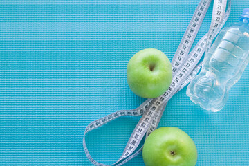 Empty space for the text. Two green apples, a measuring tape and a bottle of water on the sports mat. Top view.