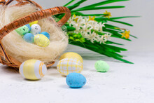 Blue And Yellow Easter Eggs On A White Concrete Table Against The Background Of A Basket With Easter Eggs And Daffodil Flowers. Selective Focus. Place For An Inscription. Close-up.