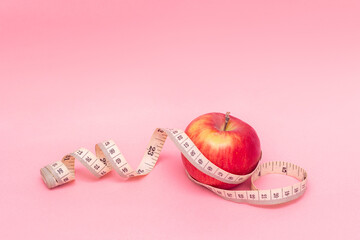 Red apple and measure tape isolated on pink background. Healthy lifestyle. Diet concept. Good nutrition