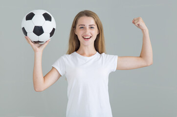 Wall Mural - Young athletic woman with a soccer ball looking at the camera. Isolated on a gray background.