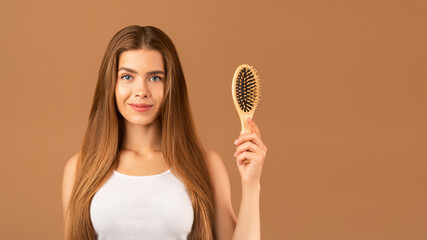 Wall Mural - Natural beauty. Attractive young woman with perfect long hair holding wooden hairbrush on brown studio background