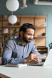 © insta_photos - Smiling bearded indian businessman working on laptop at home office. Young indian student using computer remote studying, virtual training on video call meeting, watching online webinar or seminar.