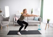 © Prostock-studio - Home training concept. Active mature lady doing squats on yoga mat indoors, copy space