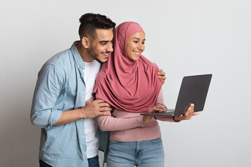 Young muslim couple using laptop computer together on grey studio background