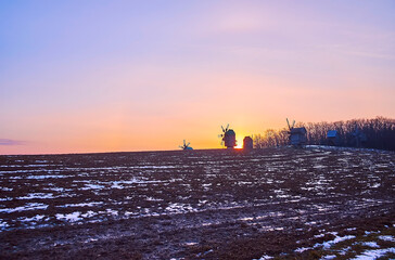 Wall Mural - The sunset over the plowed snowy field with timber windmills on horizon, Pyrohiv Skansen, Kyiv, Ukraine