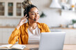 © Kateryna - Joyful contented friendly young African American woman with dreadlocks and headphones, support operator, call center employee, working at laptop, advises clients online, looking away, smiling