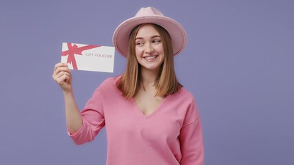 Wall Mural - Surprised joyful blonde young woman 20s years old in casual pink t-shirt hat isolated on violet purple color background studio. People lifestyle concept. Point index finger on gift certificate say wow