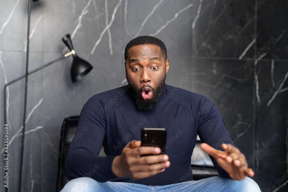 Astonished happy biracial man holding phone, looking at cellphone