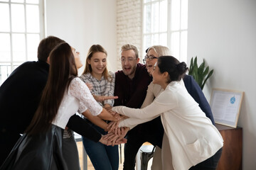 Wall Mural - Overjoyed multiethnic businesspeople join stack hands in pile involved in teambuilding activity in office. Happy diverse multiracial colleagues coworkers participate in team training at meeting.