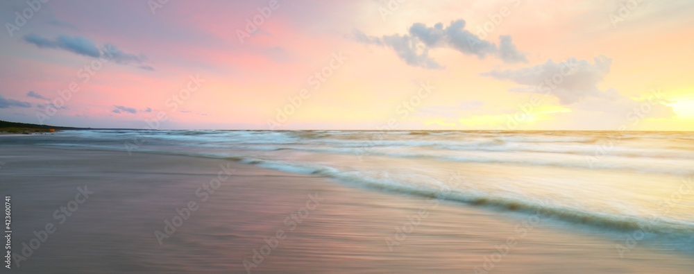 Baltic sea at sunset. Dramatic sky, blue and pink glowing clouds, soft golden sunlight. Waves, splashing water. Picturesque dreamlike seascape, cloudscape, nature. Panoramic view, long exposure - obrazy, fototapety, plakaty 