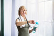 © Prostock-studio - Portrait of sporty senior woman with bottle of water checking her watch or fitness tracker indoors
