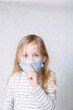 Blonde girl in striped blouse and medical mask removes the index finger to her lips