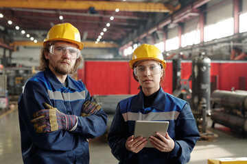 Poster - Two young serious engineers in protective workwear looking at you while standing in front of camera