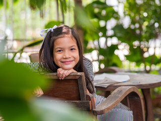 Portriat image of 8 years old Asian girl reading or doing homework at her backyard.School kid in holiday in the garden.