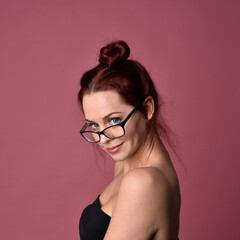 Wall Mural - Close up portrait of a red haired woman with expressive facial features and glasses on a pink studio background.