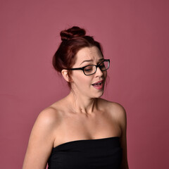 Wall Mural - Close up portrait of a red haired woman with expressive facial features and glasses on a pink studio background.