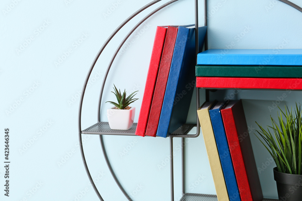 Shelf with books and houseplants hanging on color wall