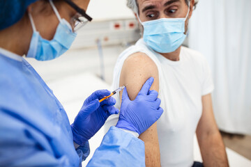 Close up of general practitioner hand holding vaccine injection while wearing face protective mask during covid-19 pandemic. Young woman nurse with surgical mask giving injection to senior man.