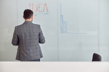 Wall Mural - Caucasian adult man in office is writing on the glass desk