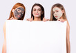 © Viorel - Facial skincare concept. Three diverse girls with different facial cosmetics mask in bath towels holding white empty blank white banner for ads near body posing over gray studio background.